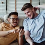men laughing while looking at the screen of a cellphone - Chat Gay Gratuita