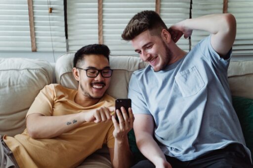men laughing while looking at the screen of a cellphone - Chat Gay Gratuita